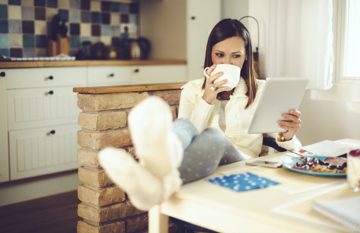 Woman sitting at table with her feet up sipping on tea reading her ipad