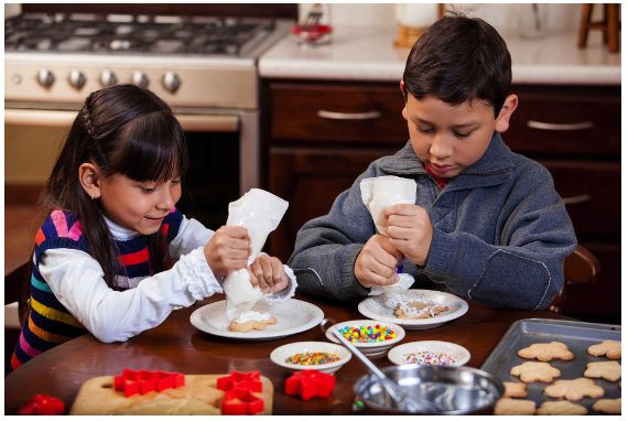 Boy and girl sitting at kitchen table decorateing holiday cookies with a smile