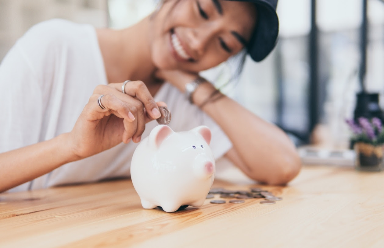Woman smiling as she places coins in her piggy bank